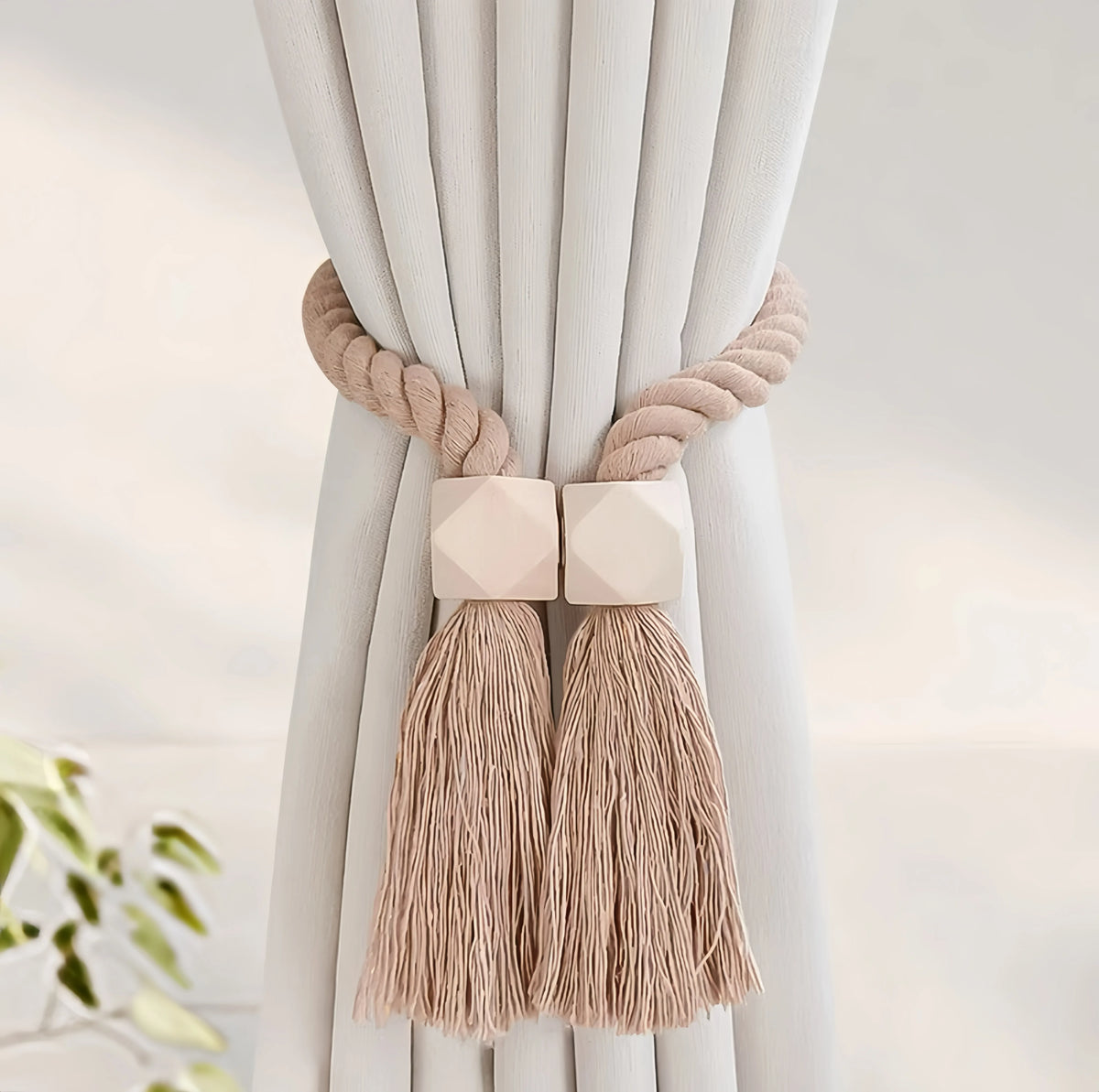 Hand-woven wooden curtain tiebacks in beige with tasseled ends tied to a white fabric drape.