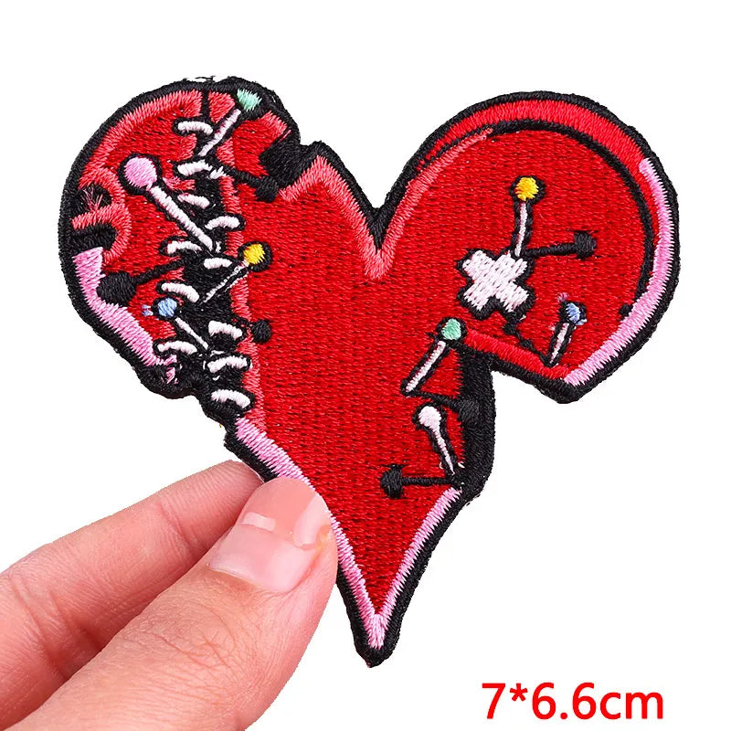 Red heart shaped embroidered patch with various colored pins and needles on a black background