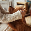 A person is hugging a soft, brown corduroy sausage dog body pillow with a cream knit sweater.
