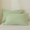 A set of three light sage green luxury brushed fabric pillowcases resting on a white bed.