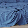 A deep blue pure linen flat sheet draped on a bed, showing soft folds and texture.
