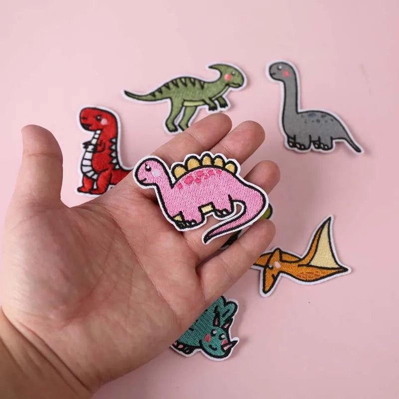 A hand holds a set of iron-on patches featuring various dinosaur and animal silhouettes.