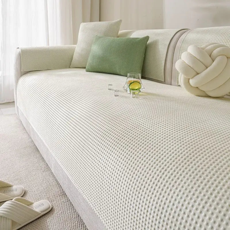 A light cream machine washable anti-slip sofa slipcover with green accent pillows and a glass of lemonade.