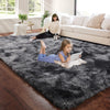 A young girl lies on a dark gray fluffy floor mat in a bright living room with a woman and a dog nearby.