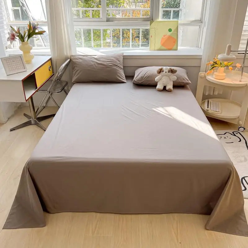 A light beige organic cotton bedding set featuring a flat sheet, pillow, and a stuffed dog toy on a bed.