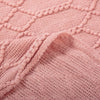 Close-up of a pink knitted throw blanket featuring a diamond pattern and a rolled cuff.