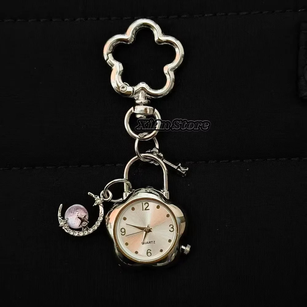 Silver pocket watch keychain featuring a round clock face and a pink charm attached to a metal loop.
