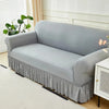 A light gray dustproof stretch sofa slipcover draped over a sofa in a bright room.