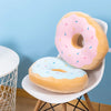 A pink and orange fried doughnut plush pillow resting on a white chair.