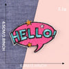 Pink embroidery patch with the word HELLO in teal stitching on a denim fabric background