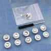 A collection of silver metal button pins laid on a translucent bag against a blue denim background.