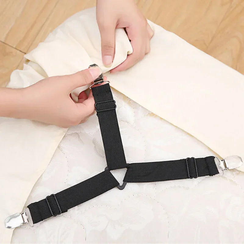 Hands are adjusting black adjustable bed sheet grippers with clips on a white fabric surface.