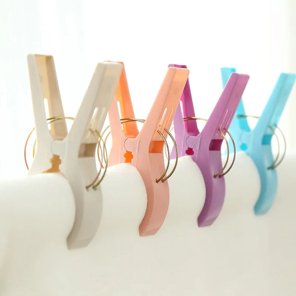A pack of four large plastic clothes pins in various pastel colors are displayed on a white surface.