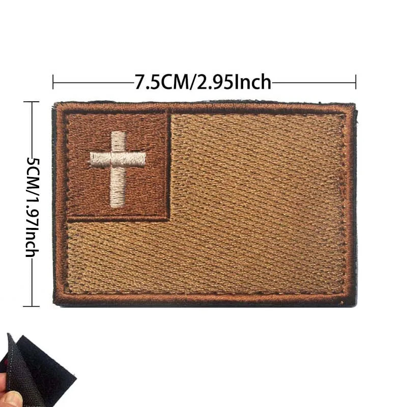 A rectangular brown embroidered patch featuring a white cross on the left and a textured field on the right.