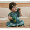 A baby wearing a teal dinosaur patterned sleeping bag is looking at a green ball.