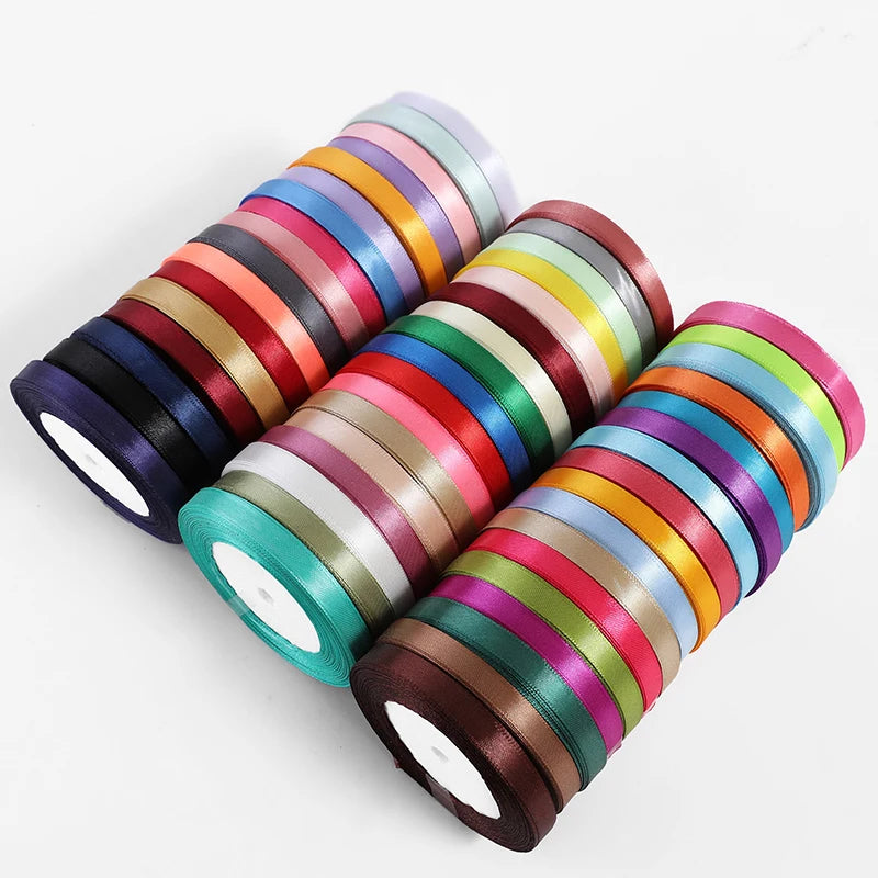 A stack of satin ribbon rolls in assorted colors, showing various shades of pink, red, green, blue, and gold.