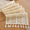 A stack of cream-colored vintage crochet lace table runners with fringe displayed on a wooden surface.