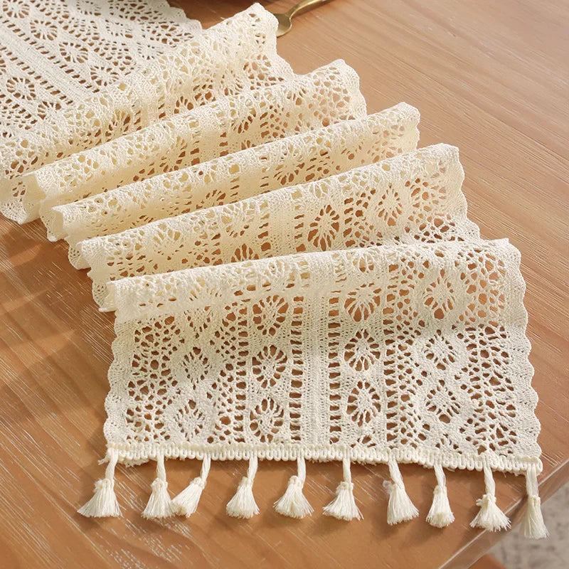 A stack of cream-colored vintage crochet lace table runners with fringe displayed on a wooden surface.