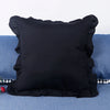 A black farmhouse ruffled pillow cover resting on a blue fabric surface.