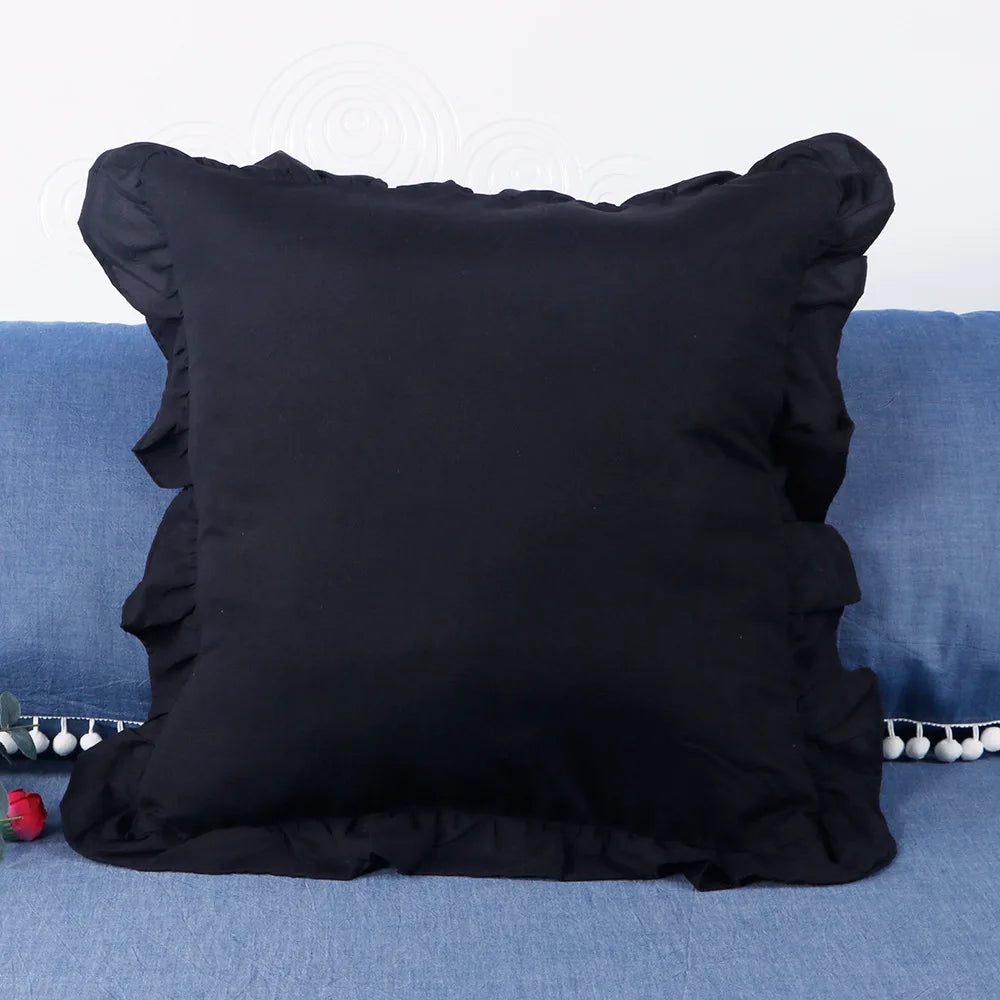 A black farmhouse ruffled pillow cover resting on a blue fabric surface.