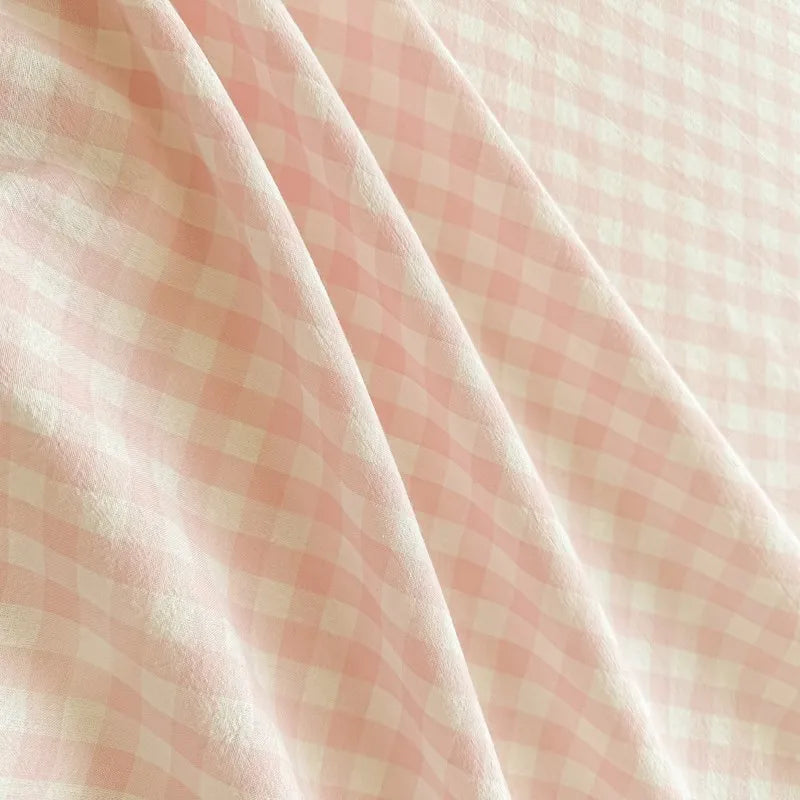 Close-up of pink gingham organic cotton bedding fabric showing a soft texture and diagonal folds.