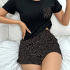 A woman wearing a black short-sleeved top and leopard print shorts in a relaxed indoor setting.