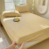 A beige flannel fitted sheet is draped over a bed, with pillows and a glass of juice visible.