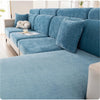 A light blue elastic sofa cover with a full backrest and cushions shown in a living room setting.