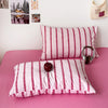 Pink striped duvet cover set with matching pillowcases and a wooden clock on a pink bed.