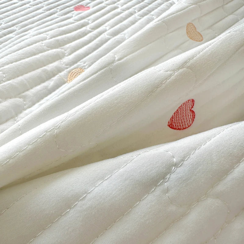 Close-up of white quilted bedding with small red embroidered hearts scattered across the fabric.