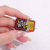 A hand holds a vintage enamel airline ticket lapel pin featuring gold lettering and an orange border.