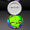 A round enamel pin featuring a stylized green face with black eyes and a red tongue against a colorful background.