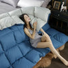 A woman relaxing on a blue quilted comforter with white pillows and a dark wooden nightstand.