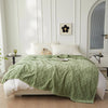 A light green plush double-sided throw blanket with a diamond jacquard pattern draped over a white bed.