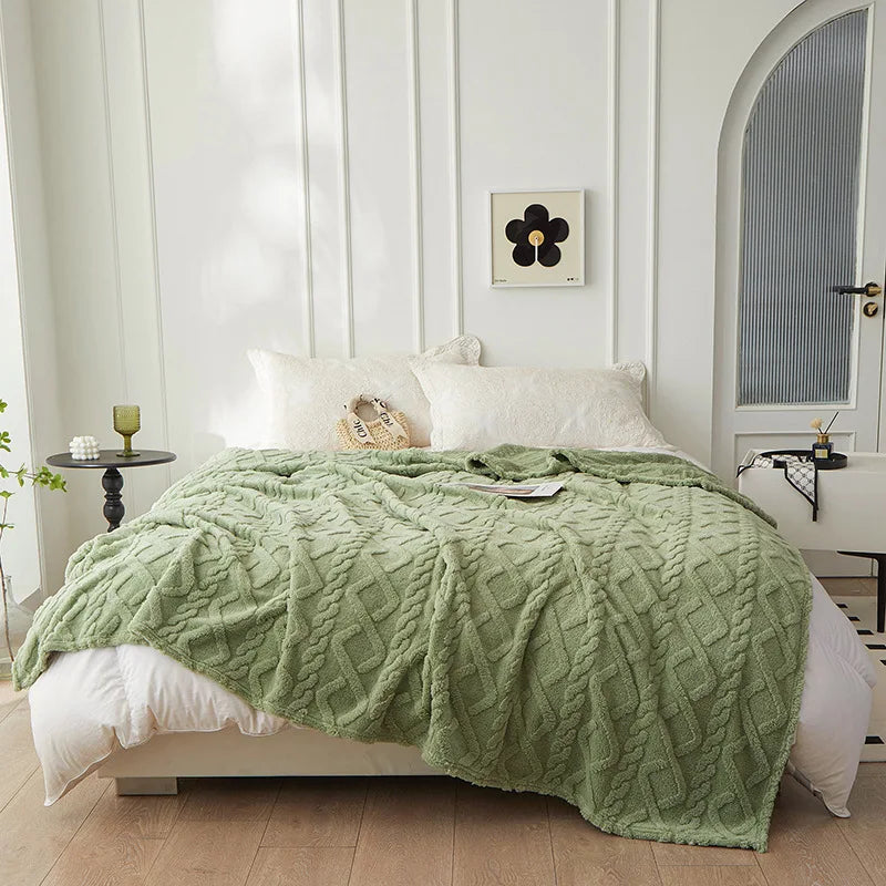 A light green plush double-sided throw blanket with a diamond jacquard pattern draped over a white bed.