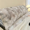 A fluffy gray plush long pillowcase resting on a bed with a white knitted blanket.