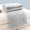 A stack of light gray quilted duvet covers and a folded duvet on a white bed.