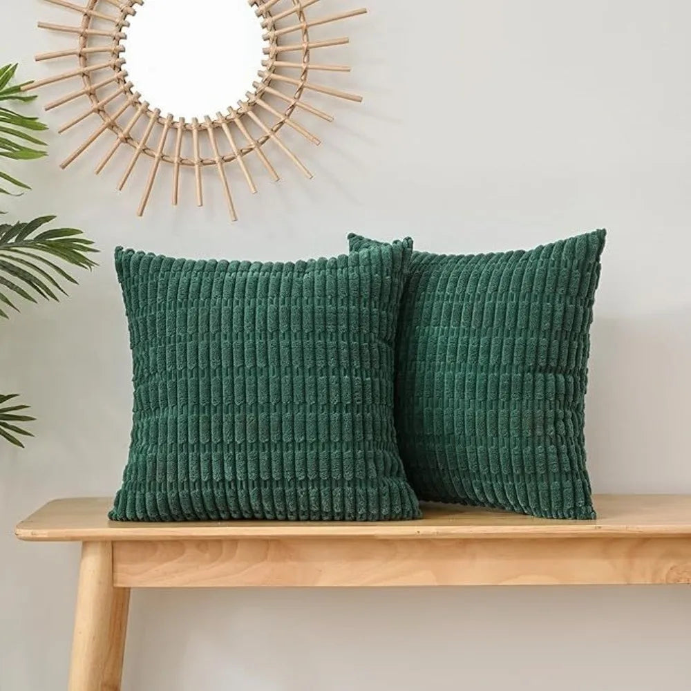 A set of two dark green, ribbed velvet throw pillow covers displayed on a wooden shelf next to a sunburst mirror.