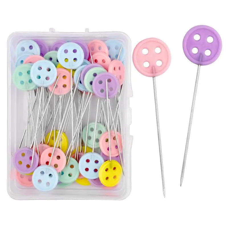 A clear plastic box containing various colored nickel-plated dressmaking pins with purple and pink heads.