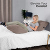 A woman is relaxing on a bed using an inflatable leg elevation pillow for comfort.