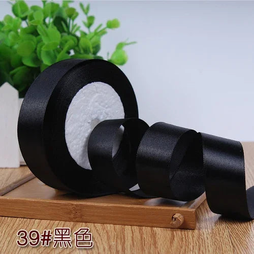 Black satin ribbon roll with white filler visible on a wooden surface.