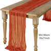 A rust orange semi-sheer gauze table runner draped over a wooden table.