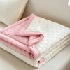 A folded pink and white waffle quilt with a quilted texture is displayed on a light-colored surface.