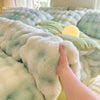 A hand touches a fluffy, light green and blue patterned fleece duvet cover with a yellow light source visible.