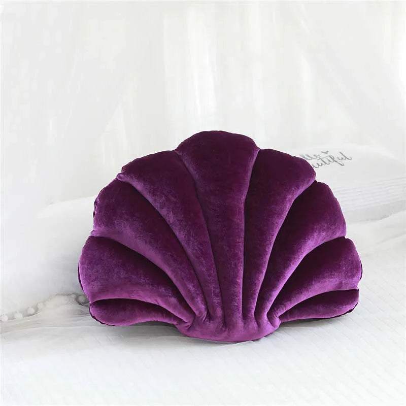 A deep purple velvet stuffed sofa cushion shaped like a decorative seashell resting on white fabric.