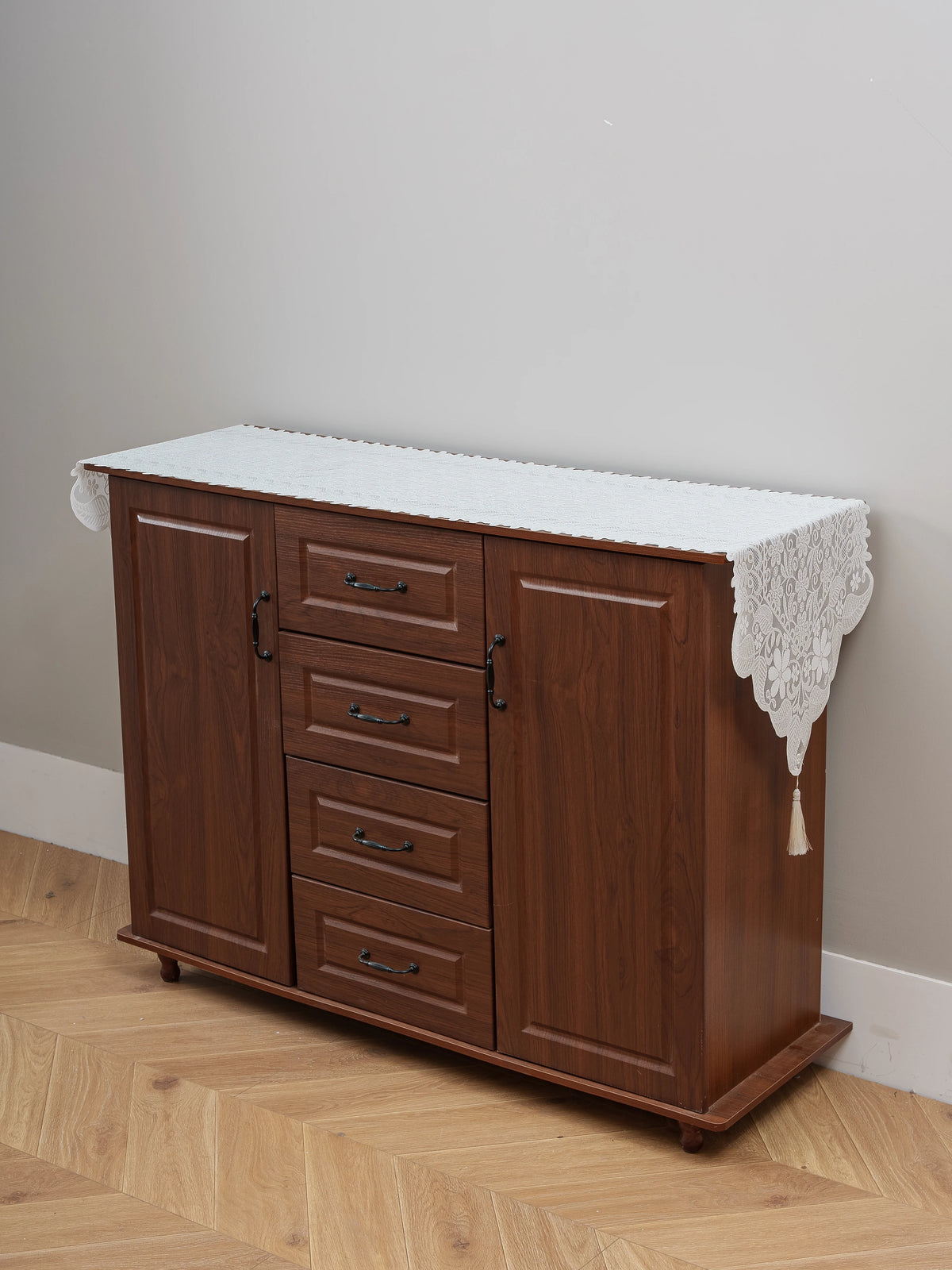 A wooden cabinet with a white embroidered lace table runner on top, used for dining or furniture accents.