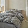 A collection of gray luxury Nordic quilt duvet covers and pillows displayed on a bed against a light wall.