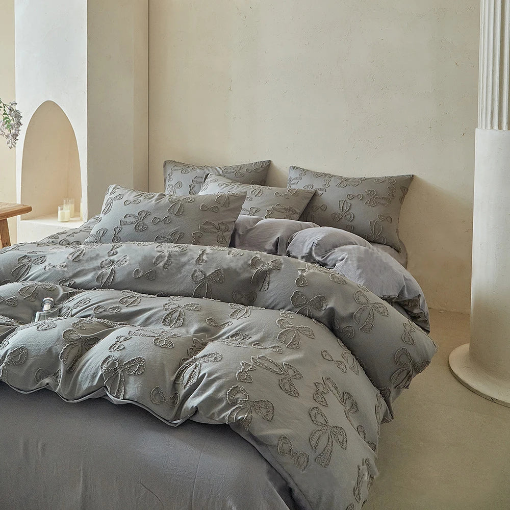 A collection of gray luxury Nordic quilt duvet covers and pillows displayed on a bed against a light wall.
