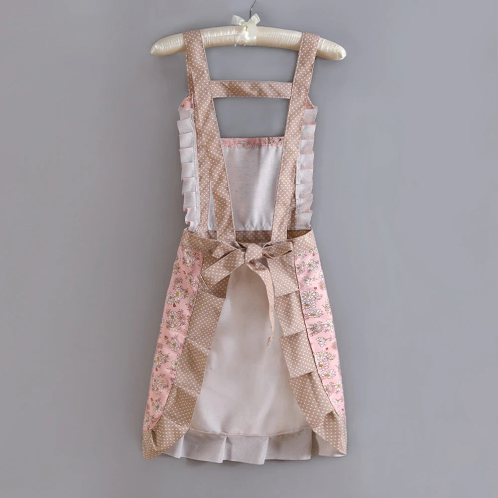 A light pink floral pattern kitchen apron with adjustable straps hanging on a wooden hanger.