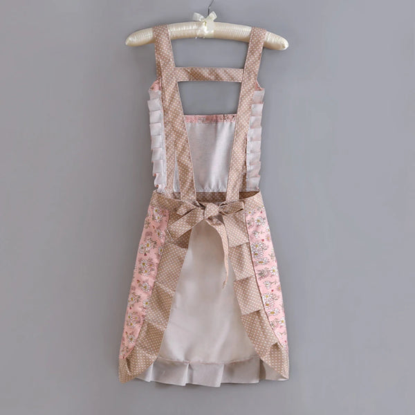 A light pink floral pattern kitchen apron with adjustable straps hanging on a wooden hanger.